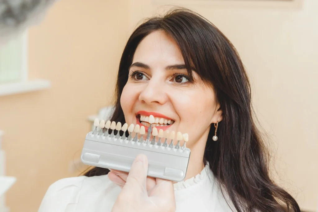 Woman smiling while holding a dental shade guide to compare tooth color options for veneers.