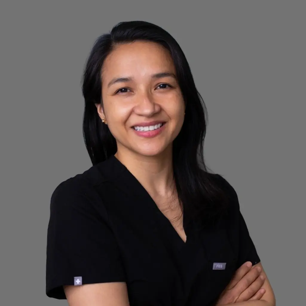 Female dentist in black scrubs smiling at Great Neck dental practice.