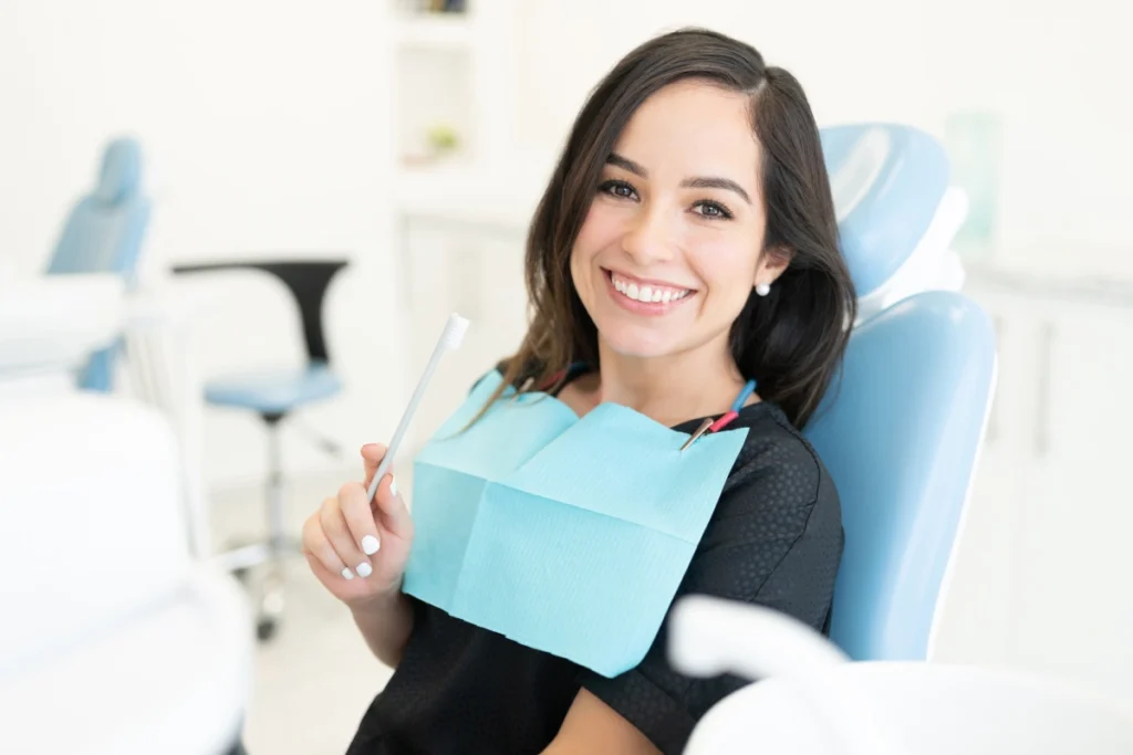 Smiling woman in dental chair holding mirror, demonstrating confidence and oral health results.