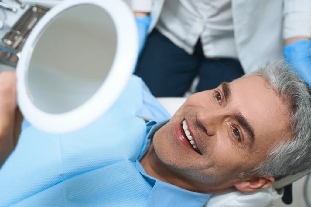 Man examining his smile in mirror at dental office in Great Neck.