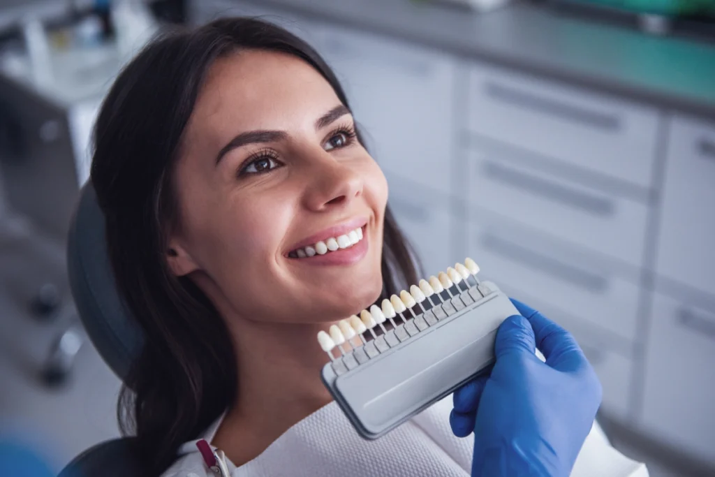 Woman smiling while holding a dental shade guide to compare tooth color options for veneers.