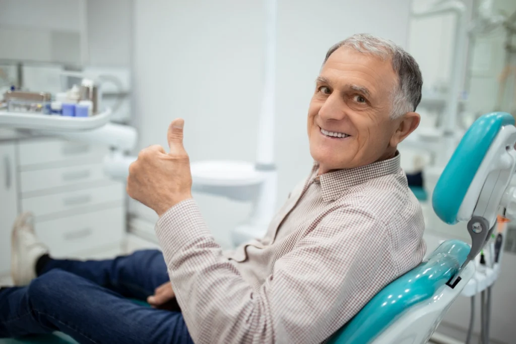 Mature male patient giving thumbs up in dental chair at Great Neck practice.