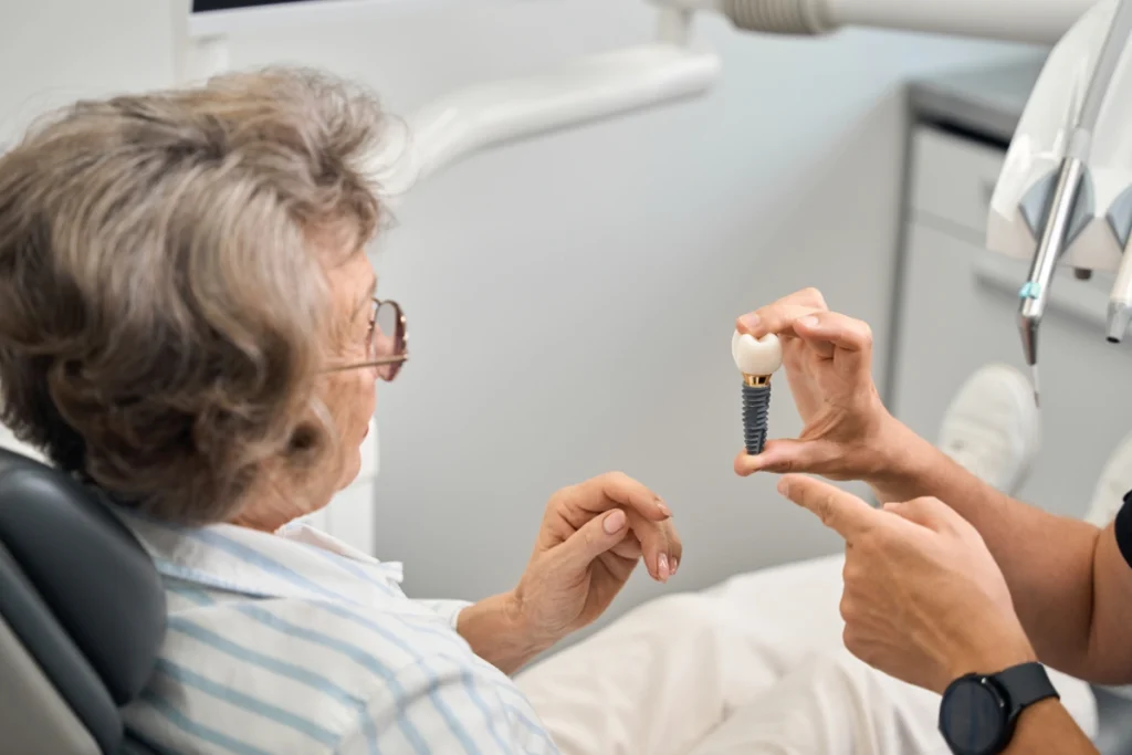 Dentist showing dental implant model to senior patient during consultation.