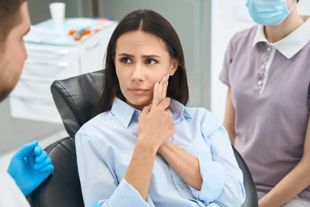 Woman with tooth pain holding her cheek during dental consultation at Great Neck office.