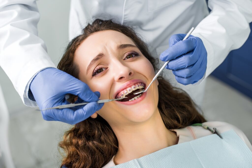 Dentist examining patient's teeth with braces during cosmetic dental treatment in Great Neck.